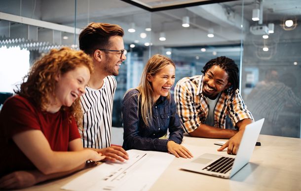 Image of startup friends laughing around a laptop on a desk